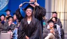 Zoom image: student getting hooded on stage. 