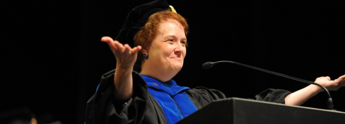 Dean Nancy Smyth at commencement in regalia, happy, hands up facing the audience. 
