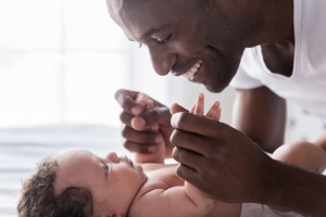 Dad grasps his baby's hands and smiles. 