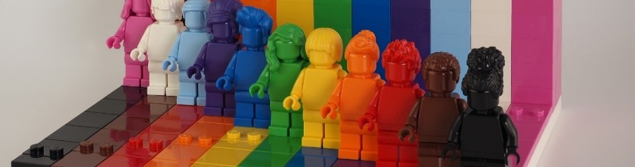 Pink, white, light blue, navy blue, royal blue, green, yellow, orange, red, brown, and black Lego figurines standing side by side. 