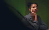 Black woman with elbow on desk and resting her head in her hands looking unhappy. 
