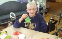 Elderly woman holding up handmade frog ornament. 