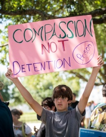 Boy holding poster stating Compassion Not Detention. 