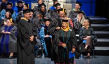 Zoom image: student being hooded on stage.