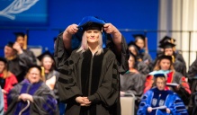 Zoom image: PhD student being hooded on stage.
