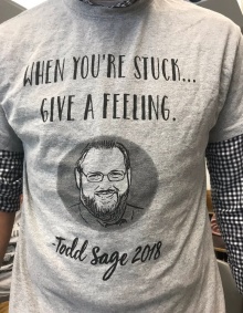 Close-up of t-shirt that says "when you're stuck...give a feeling" - Todd Sage 2018, with an illustration of Todd Sage's face. 