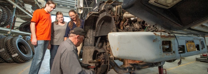 Students with mechanic working on truck engine.