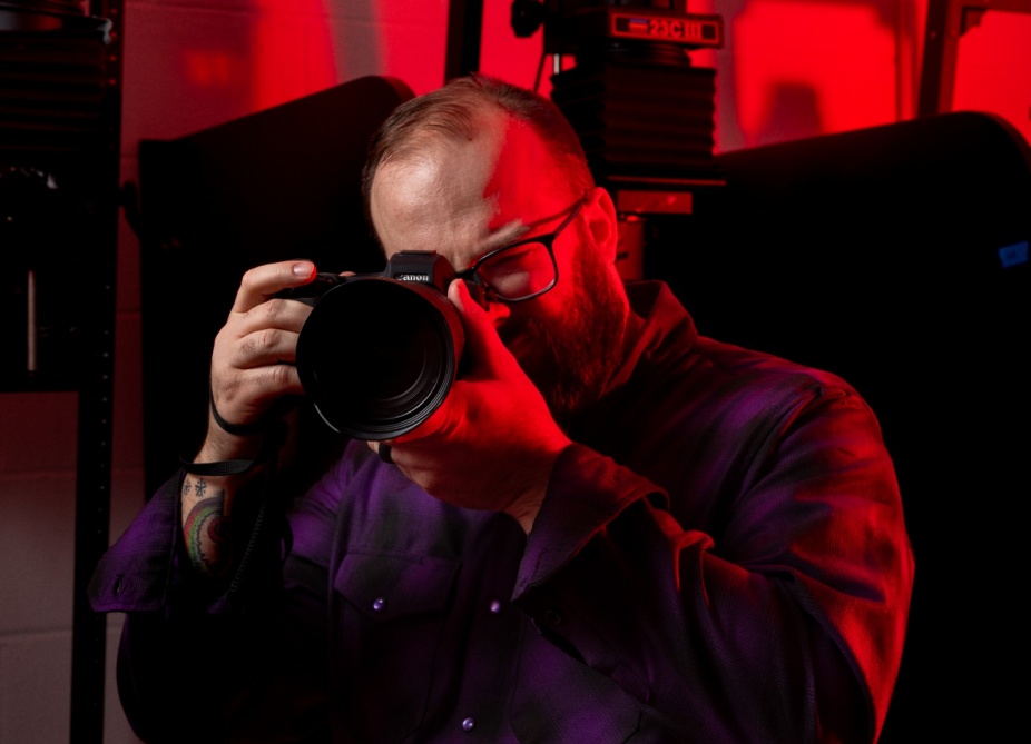 Rob Healy pointing his camera while in a photography darkroom.