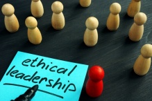 Post-It Note with the phrase "Ethical Leadership!" written in Sharpie, next to a red boardgame piece place in front of several beige boardgame pieces creating the effect of a speaker with an audience. 