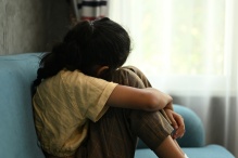 Young girl sitting on a couch curled up holding her knees. Meant to indicate sadness. 